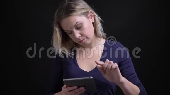 金发女商人穿着蓝色衬衫在黑色背景下认真地用平板手表对着相机工作视频的预览图