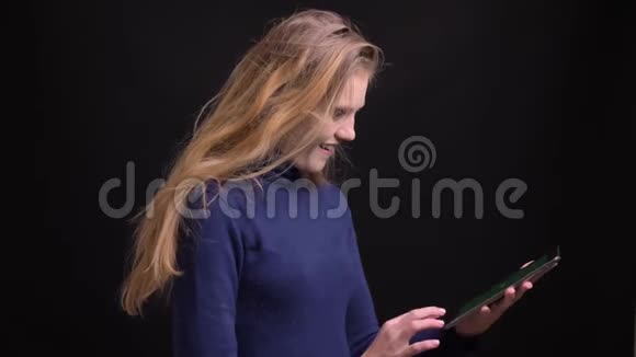 年轻的金发模特开始在平板电脑上的应用程序并显示其绿色屏幕以愉快的相机在黑色背景视频的预览图
