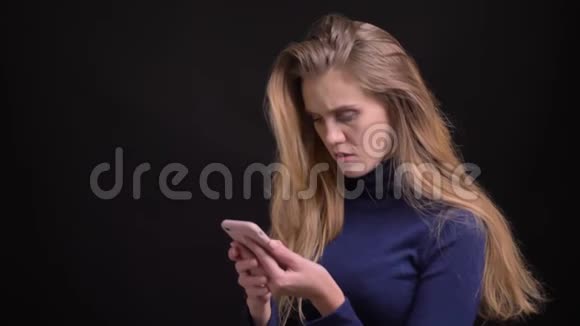 一位年轻的金发模特正在使用智能手机她抬头看着镜头在黑色背景下微笑着进入镜头视频的预览图