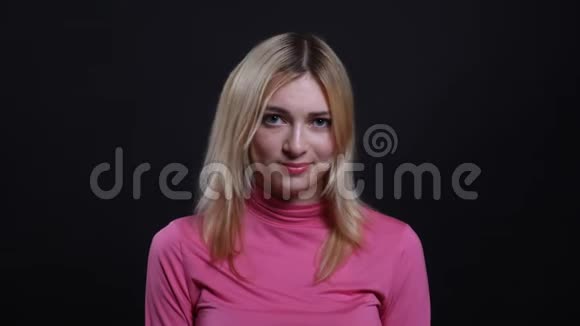 年轻漂亮的金发女性的特写镜头带着害羞和困惑的微笑看着背景的相机视频的预览图