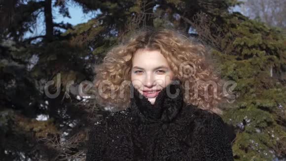 突然雪飞到女孩的脸上一个穿着黑色外套的卷发女孩在一个阳光明媚的寒冷的冬天视频的预览图