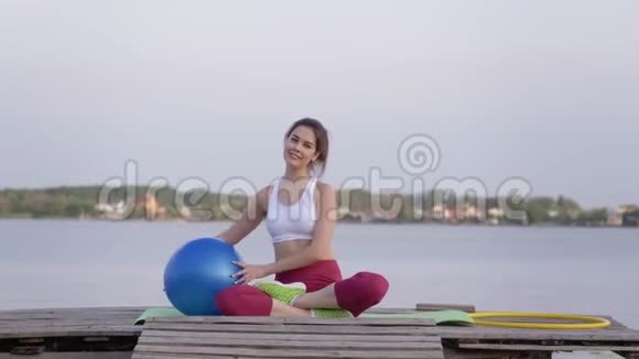 健康的微笑女孩在大自然的木桥上坐在垫子上做手臂肌肉锻炼视频的预览图
