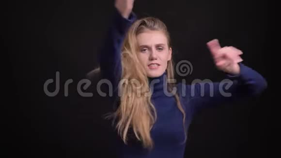 年轻的金发模特穿着蓝色毛衣在黑色的背景下欢快而积极地跳舞视频的预览图