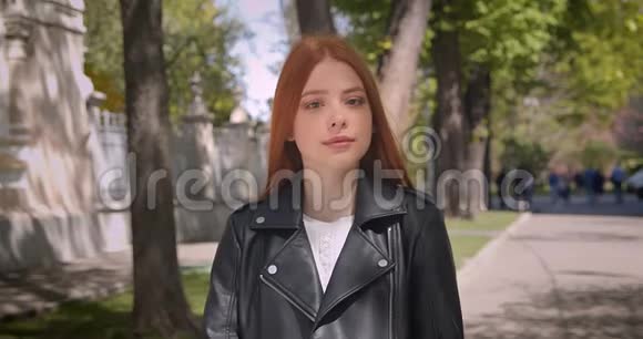 漂亮的生姜模特穿着皮夹克开心地笑着进入相机调整她的头发公园背景视频的预览图