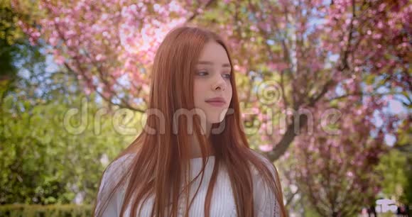 迷人的姜女学生穿着白色衬衫迷人地摆在粉红色花圃的相机里视频的预览图