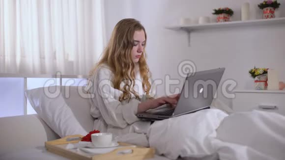 穿长袍的女孩在床上喝咖啡在笔记本电脑上工作自由职业概念视频的预览图