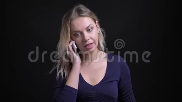 金发女商人穿着蓝色衬衫带铲子领口在黑色背景的智能手机上有非正式的语音信箱视频的预览图