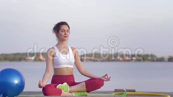 瑜伽的生活方式美丽的瑜伽女子在莲花的位置冥想和享受精神平静的近水视频的预览图