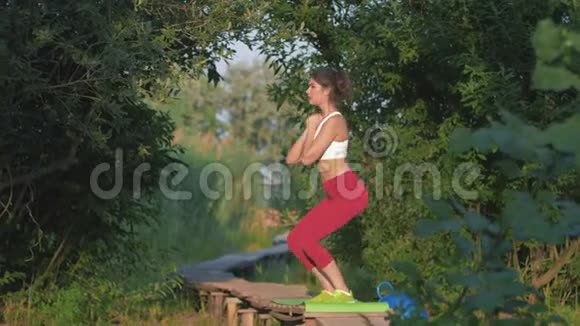 体育活动令人惊奇的女孩在木制桥上露天锻炼时进行运动蹲式锻炼视频的预览图