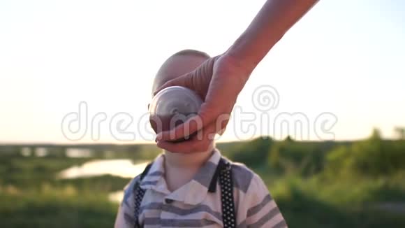 小男孩正在慢慢地喝着妈妈在日落时拿着的婴儿奶瓶视频的预览图