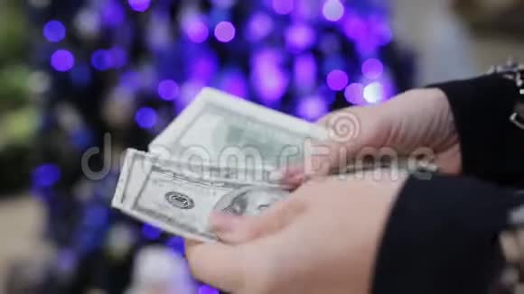 女人的手在圣诞树的背景上数着美元是时候买节日礼物了视频的预览图