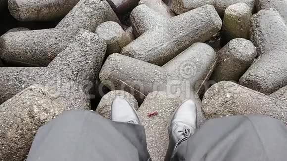 一个穿着正式办公服的男人坐在岩石上看着他的腿和海岸之间的螃蟹享受着连绵的海浪视频的预览图