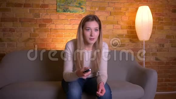 年轻有魅力的白种人深色头发的女性在看体育电视坐在沙发上开心的特写镜头视频的预览图