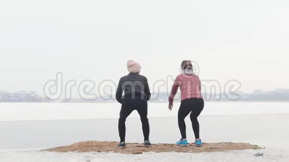 两个穿着夹克的苗条女人在雪地海滩上蹲着弯腰视频的预览图