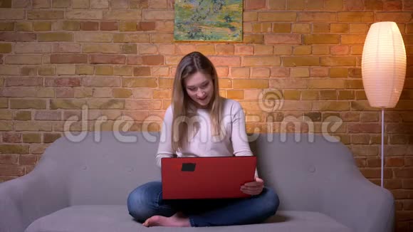 年轻迷人的白种人深色头发的女性特写镜头她在笔记本电脑上看一部有趣的电影开心地笑着视频的预览图