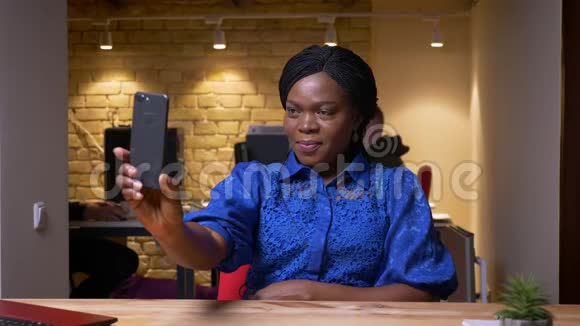 一位成年非裔美国女商人坐在笔记本电脑前用手机自拍的特写镜头视频的预览图