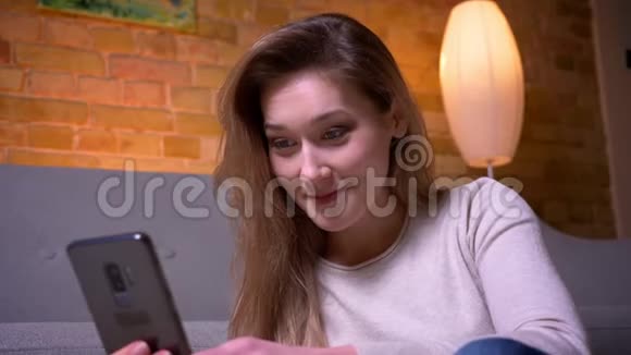 年轻迷人的白种人深黑肤色的女性在手机上浏览社交媒体的特写镜头坐在地上视频的预览图