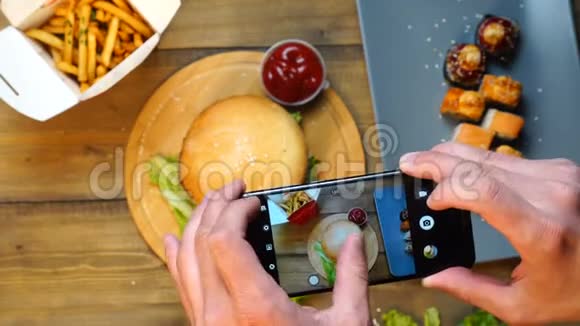 时髦的男人用她的智能手机拍摄新鲜美味的大汉堡午餐照片分享她的社交社区视频的预览图