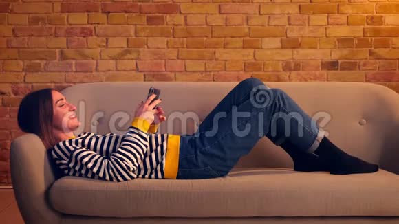特写侧景照片年轻漂亮的女孩用电话兴高采烈地躺在沙发上悠闲地躺在沙发上视频的预览图