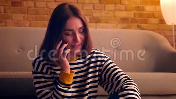 一张年轻漂亮女孩的特写照片她打了个电话兴高采烈地坐在一个舒适的地板上聊天视频的预览图