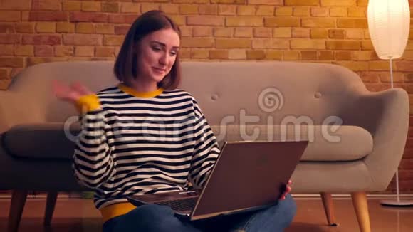 一张年轻漂亮女孩的特写照片她在笔记本电脑上打了一个视频电话高兴地坐在电脑上挥着微笑视频的预览图