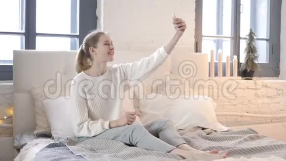 幸福的女人坐在床上用电话自拍照片视频的预览图