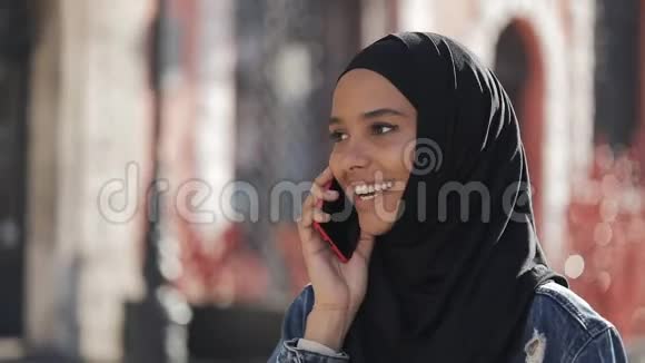在城里一位戴着头巾的穆斯林年轻女士微笑着用智能手机与朋友交谈一位女士走在路上视频的预览图