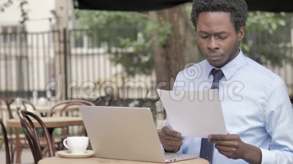 非洲商人在户外咖啡厅边看文件视频的预览图