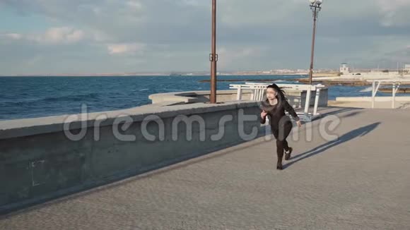 穿着黑色运动服的年轻迷人女子沿着海岸慢跑视频的预览图