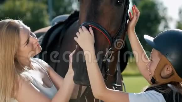 母女骑手和骑师在绿色的田野拥抱一匹棕色的马视频的预览图