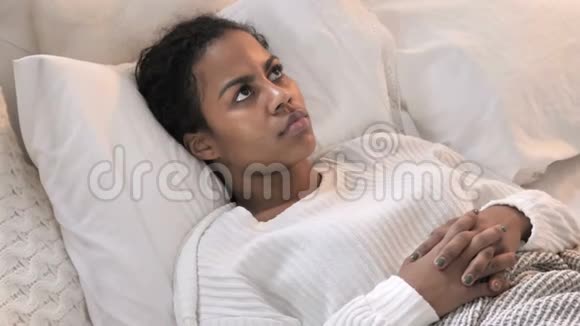年轻的非洲妇女躺在床上的痛苦思考的最高视角视频的预览图