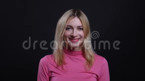 年轻漂亮的金发女郎穿着一件粉红色毛衣微笑着可爱地看着背景镜头的特写镜头视频的预览图