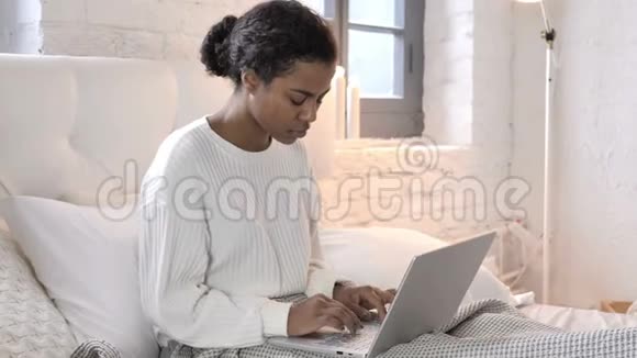 疲惫的非洲年轻女子颈部疼痛在床上工作视频的预览图