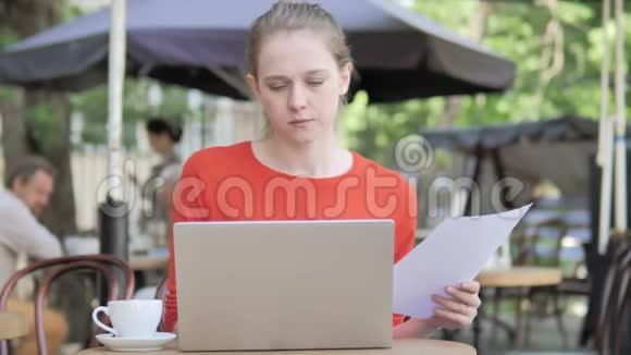 年轻女子阅读合约及使用电脑坐在咖啡厅露台视频的预览图
