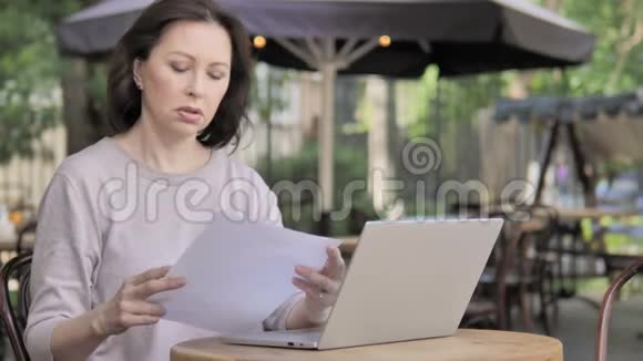老年妇女阅读文件坐在户外咖啡厅视频的预览图
