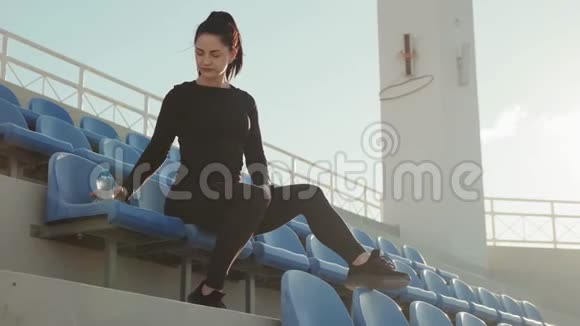 穿黑色运动服的年轻女士坐在蓝色的椅子上早上锻炼后喝水户外慢动作视频的预览图