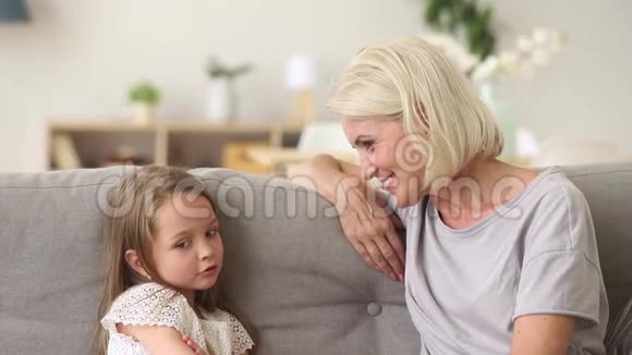 可爱的小孙女和奶奶聊天坐在沙发上玩得很开心视频的预览图