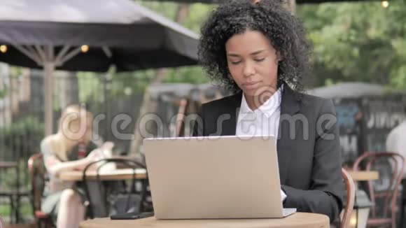 咳嗽的非洲女商人在户外咖啡厅做手提电脑视频的预览图