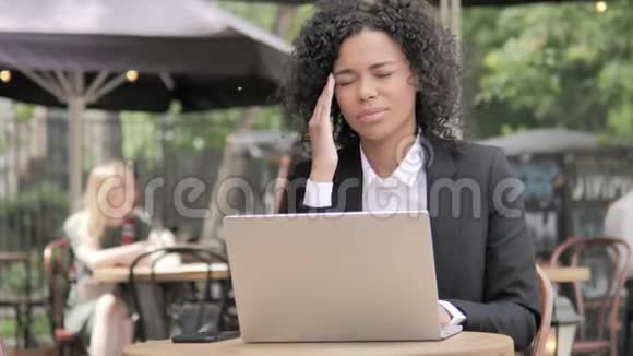 带头疼的非洲女商人在户外咖啡厅使用笔记本电脑视频的预览图