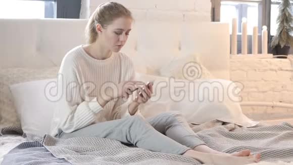 坐在床上的年轻女子通过智能手机进行网上购物视频的预览图