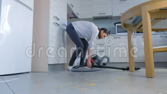 女人用吸尘器打扫厨房地板她整理了散落在灰色瓷砖上的玉米片视频的预览图