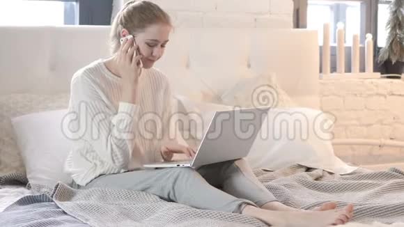 女人在床上和使用笔记本电脑时讲电话视频的预览图
