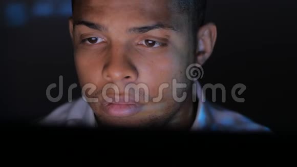 非裔美国人英俊的商人用电脑做工作程序员晚上认真看监控屏幕视频的预览图