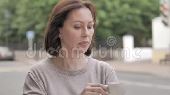 户外坐着的老女人喝咖啡视频的预览图
