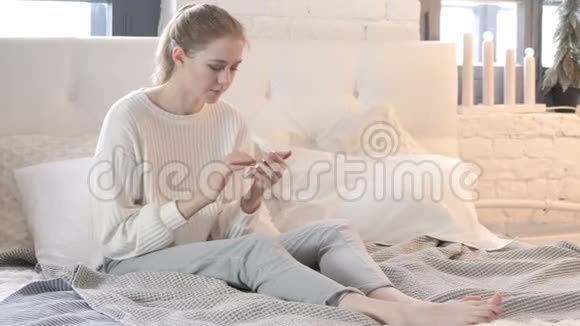 情绪激动的女人坐在床上对智能手机的失败作出反应视频的预览图