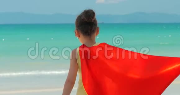 可爱的小女孩穿着超级英雄的服装穿着红色斗篷和英雄的面具出现在背景海上视频的预览图