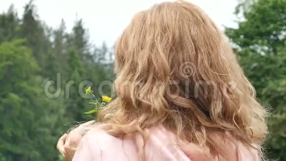 美丽卷曲的红发女人手里拿着一朵黄色的野花反对森林和山脉的肖像夏季视频的预览图