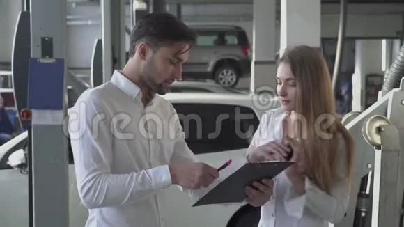 英俊的男经理告诉漂亮的客户如何填写机器维修合同并在汽车服务中领取钥匙视频的预览图