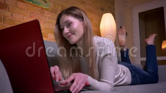 在笔记本电脑上给年轻有魅力的白种人深色头发的女性发短信并快乐地听音乐视频的预览图