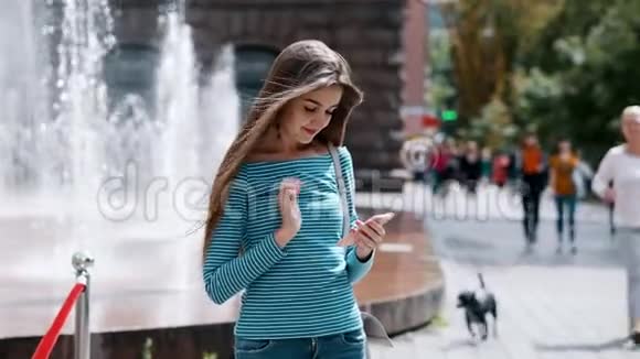 年轻时尚的女孩在城市街道上使用智能手机一个女人打印一条信息聊天视频的预览图
